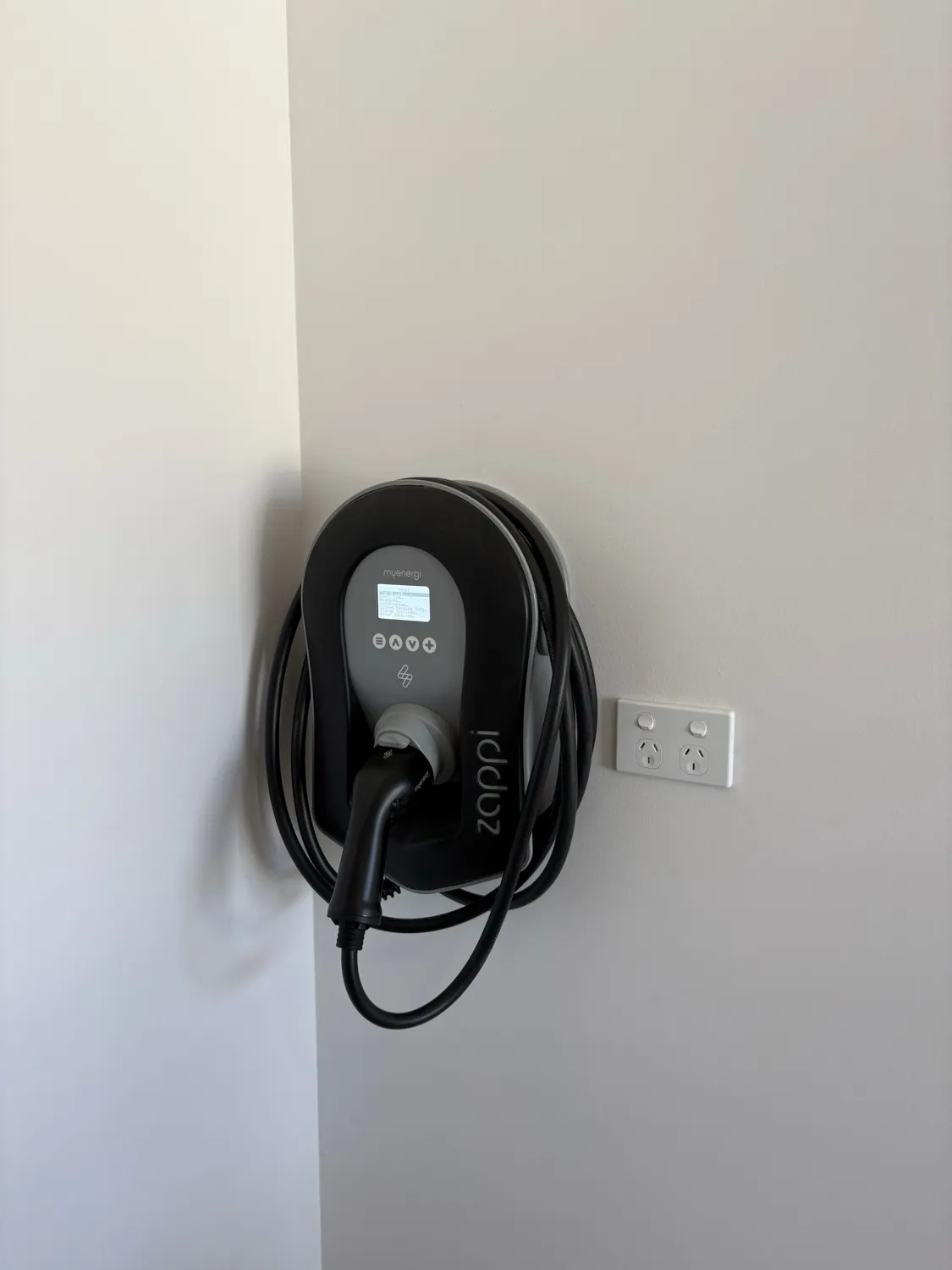 Black Zappi EV charger neatly installed in a corner beside a power point